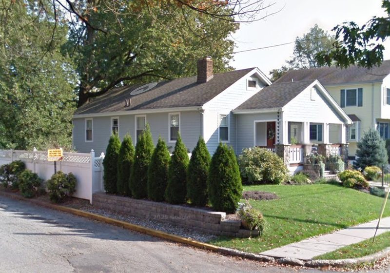 Cape-style home behind a row of evergreens in Metuchen, NJ